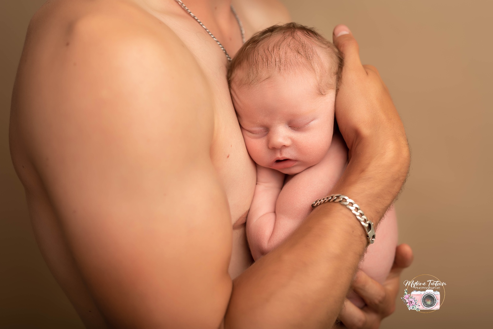 bébé dans les bras de papa en peau a peau possible au studio pendant la séance 